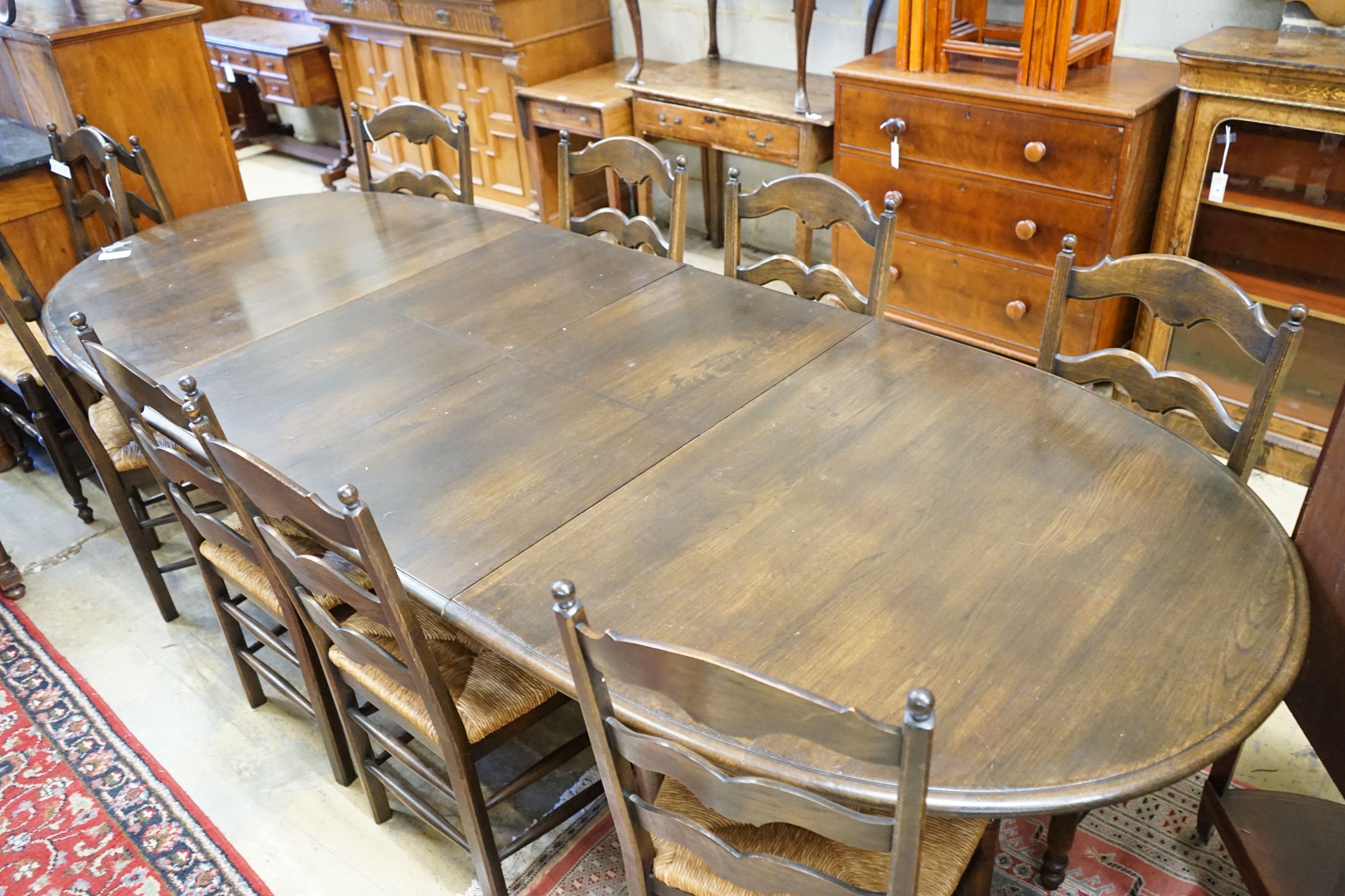 A French style oak extending dining table, with two spares leaves, 280cm extended, width 11cm, height 74cm together with a set of ten ladder backed rush seated chairs